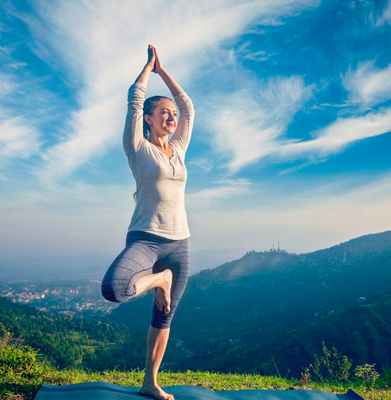 Женщина стоит на одной ноге на фоне гор и природы