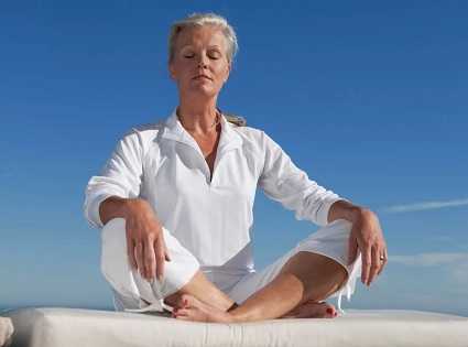 Пятидесятилетняя женщина медитирует на берегу моря