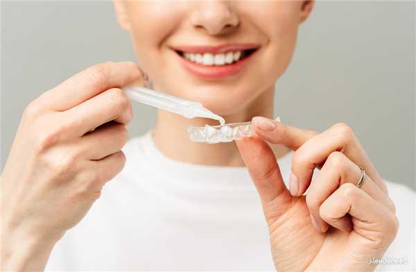 молодая женщина делает процедуру отбеливания зубов в домашних условиях