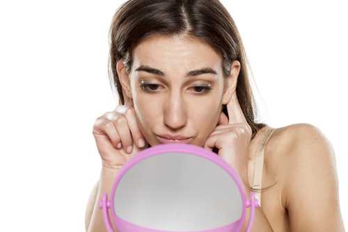 девушка смотрит на свои уши в зеркало